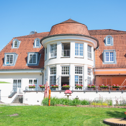 Haus mit runder Veranda, Satteldach und Blumenkästen an den Fenstern.