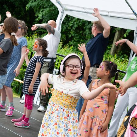 Gruppe von Kindern und Erwachsenen, die auf einer Bühne tanzen und sich freuen.