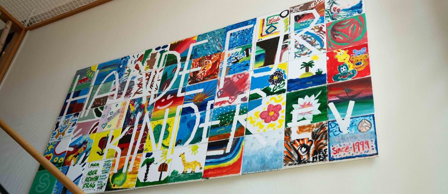 Ein buntes Bild hängt an der Wand an der Treppe zur Kinderetage im Neuen Kupferhof. Das Bild ist ein Mosaik, bestehend aus vielen einzeln bemalten Leinwänden.