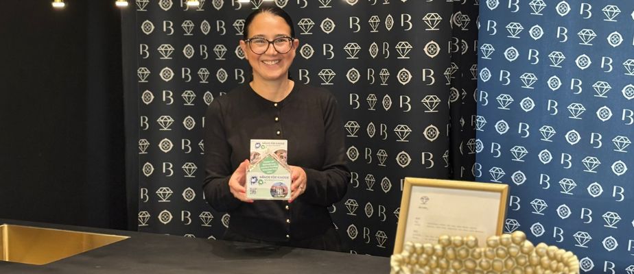 Eine lachende Frau hält eines unserer kleinen Spendenhäuser in der Hand. Sie steht vor einem dunklen Hintergrund.