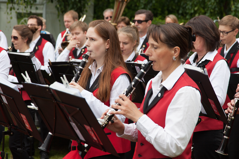 Musikerinnen und Musiker eines Blasorchesters spielen Klarinetten in roten Westen und weißen Hemden.
