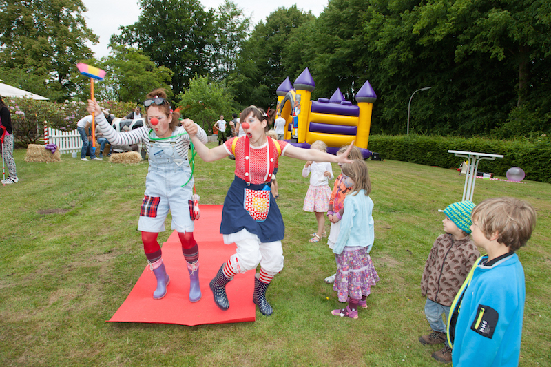 Zwei Clowns in bunten Kostümen tanzen auf einem roten Teppich während einer Veranstaltung im Freien.