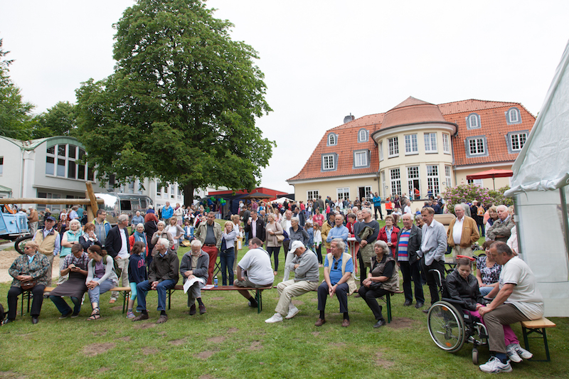 Eine große Menschenmenge versammelt sich auf einer Wiese während einer Veranstaltung mit einem historischen Gebäude im Hintergrund.
