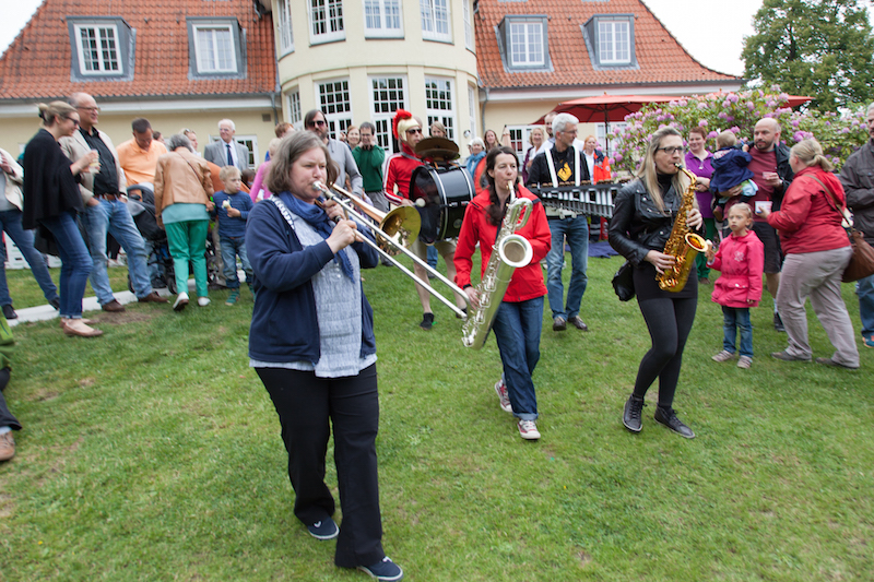 Eine Gruppe von Musikerinnen, die mit verschiedenen Blasinstrumenten auf einem Rasen spielt.