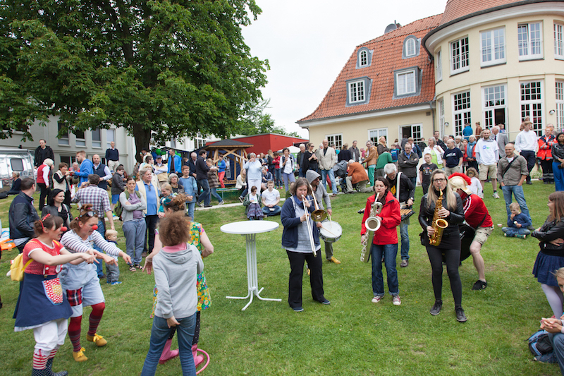 Eine Gruppe von Menschen bei einem Fest, darunter Musiker mit Instrumenten und tanzende Personen.