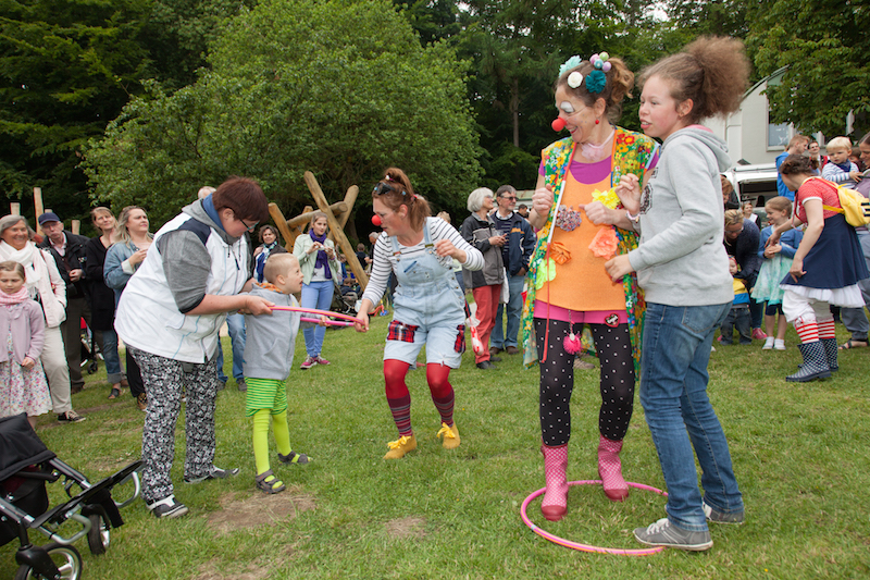 Clown in bunter Kleidung spielt mit Kindern während einer Veranstaltung im Freien.
