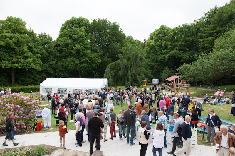 Eine große Menschenmenge versammelt sich bei einer Veranstaltung im Freien, umgeben von Bäumen und einem Zelt.