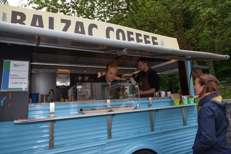 Kaffeewagen mit dem Namen Balzac Coffee und zwei Baristas, die mit einer Kundin sprechen.