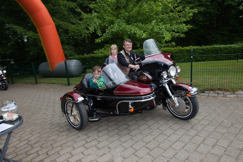 Ein Motorrad mit Beiwagen, auf dem zwei Kinder und ein Erwachsener sitzen.