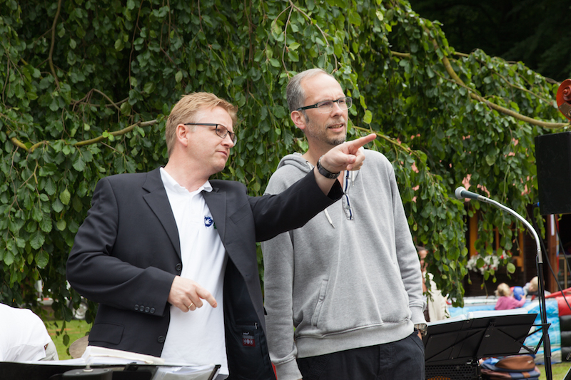 Zwei Männer stehen nebeneinander und zeigen auf etwas während einer Veranstaltung im Freien.