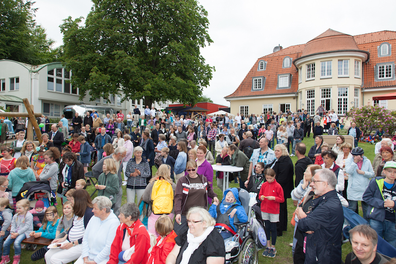Eine große Menschenmenge versammelt sich auf einer Wiese während einer Veranstaltung vor einem Gebäude.