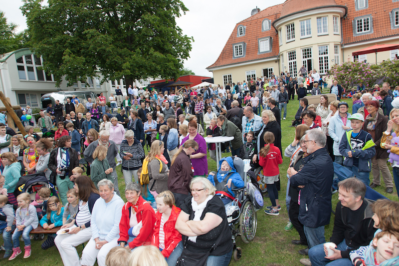 Eine große Menschenmenge versammelt sich auf einer Wiese während einer Veranstaltung vor einem Gebäude.