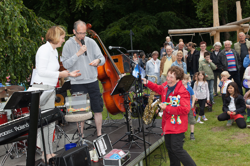 Ein Mann und eine Frau stehen auf einer Bühne im Freien, während Publikum zuschaut.