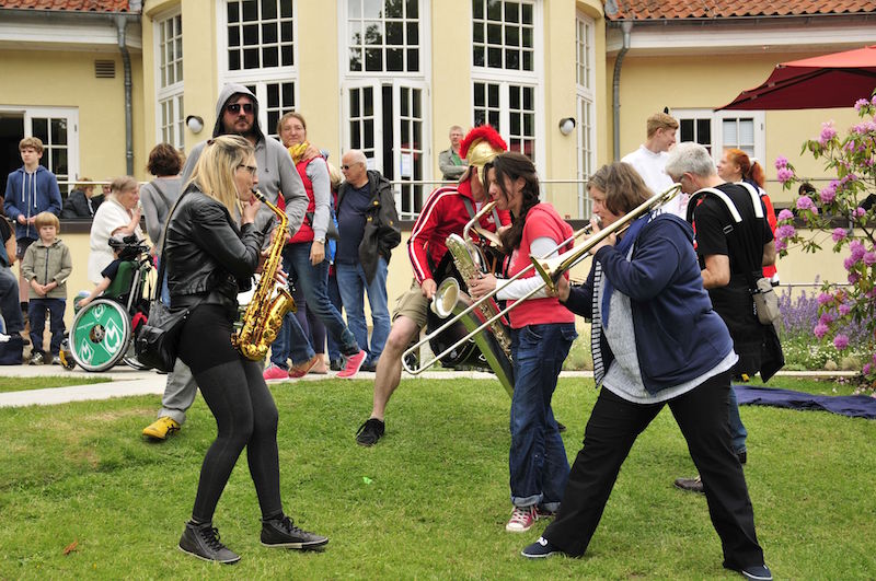 Eine Gruppe von Musikerinnen spielt Blasinstrumente im Freien, während Menschen um sie herum stehen.