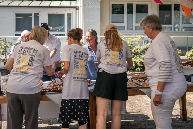 Gruppierung von Personen in T-Shirts, die an einem Tisch mit Speisen bei einem Sommerfest stehen.