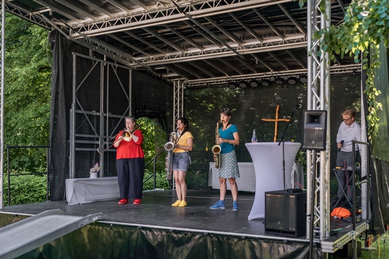 Vier Musikerinnen auf einer Bühne, die verschiedene Instrumente spielen, darunter Trompete und Saxophon.