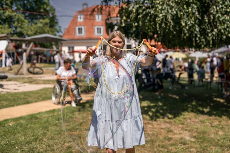 Eine Frau in einem hellen Kleid, die sehr große Seifenblasen macht.