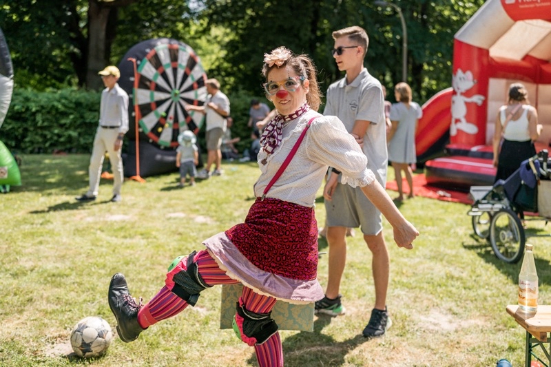 Clownin mit buntem Kostüm und Schminke, die einen Ball schießt.