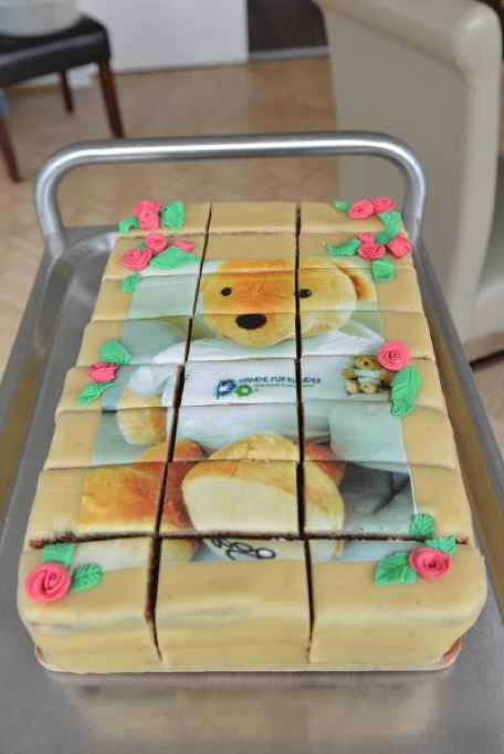 Ein rechteckiger Kuchen mit einem Bärenmotiv, dekoriert mit Rosen und Blättern aus Zucker.