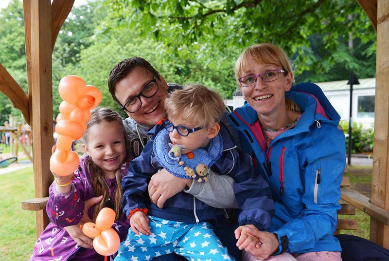 Eine Familie mit zwei Kindern, die orangefarbene Ballons halten und im Freien sitzen.