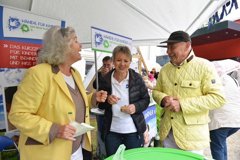 Drei Personen stehen an einem Stand von Hände für Kinder während einer Veranstaltung.