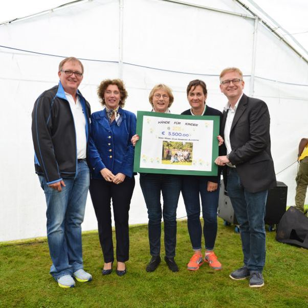 Fünf Personen halten einen großen Scheck über 5500 Euro in einem Zelt.