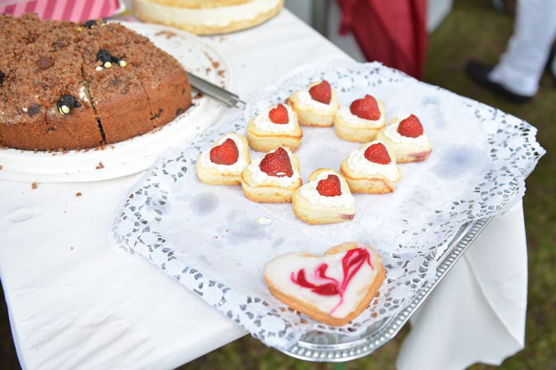 Ein Tablett mit herzförmigen Erdbeertörtchen und einem großen Keks mit rotem Muster.