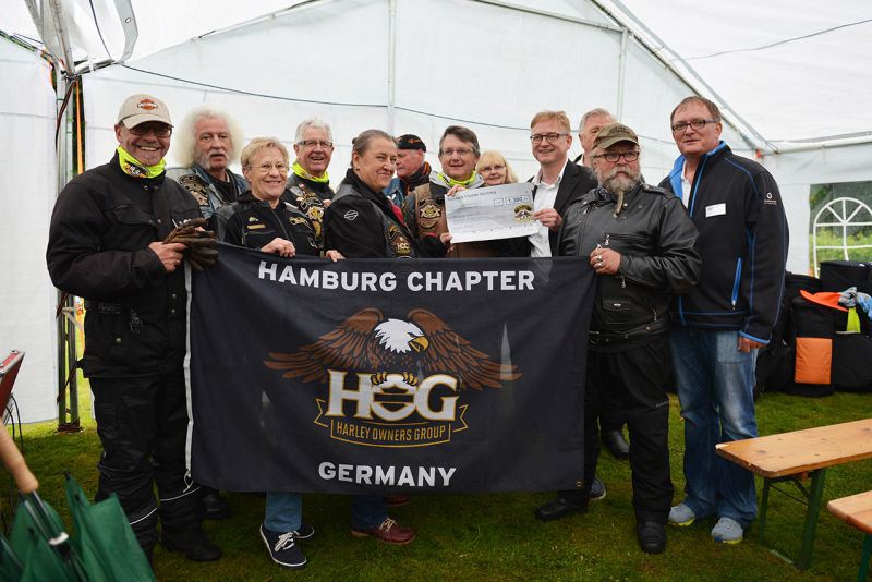 Gruppe von Personen mit Harley-Davidson-Kleidung, die ein Banner der Harley Owners Group Hamburg Chapter halten.
