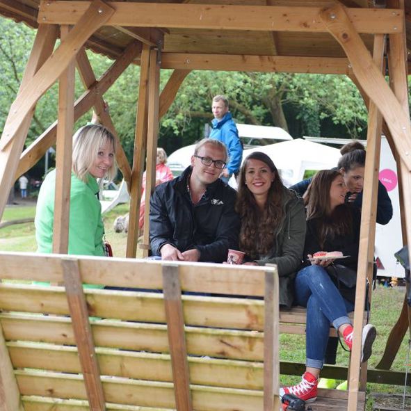 Vier Personen sitzen auf einer Holzbank unter einem Pavillon im Freien.