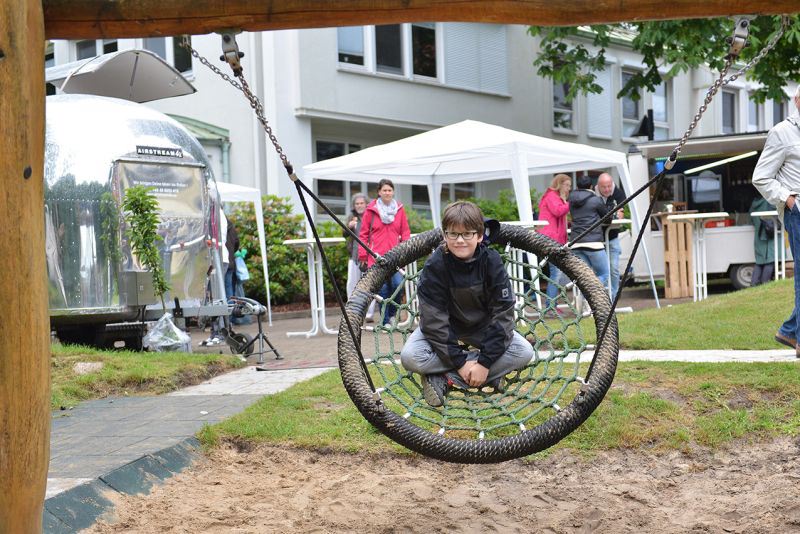 Ein Kind sitzt auf einer Nestschaukel, umgeben von Menschen und Zelten.