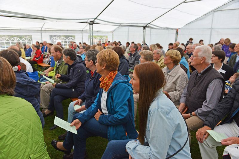 Eine große Gruppe von Menschen sitzt in einem Zelt und hört einer Veranstaltung zu.
