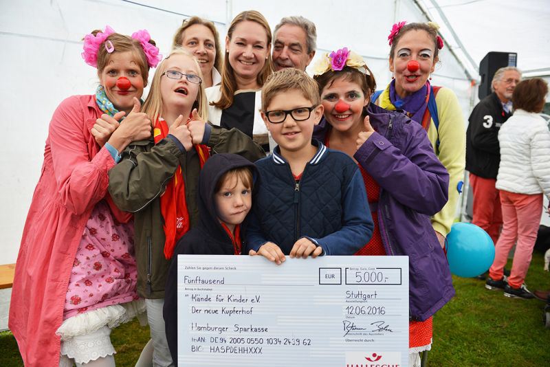 Eine Gruppe von Menschen, darunter Clowns, posiert mit einem großen Scheck für eine Spende.