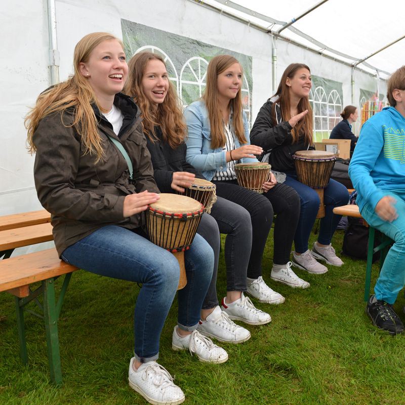 Vier Jugendliche sitzen auf Bänken und spielen Trommeln in einem Zelt.