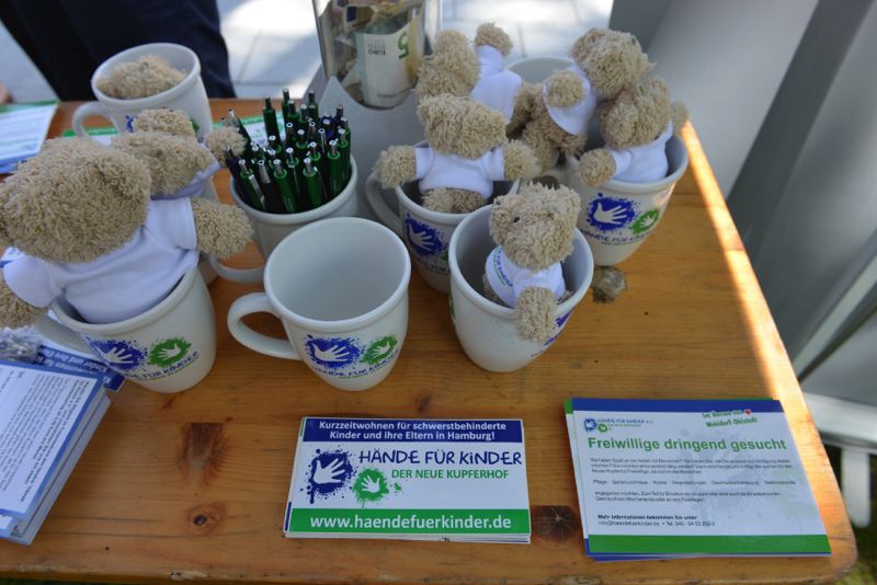 Mehrere Teddybären in Tassen, die auf einem Tisch stehen, umgeben von Stiften und Informationsmaterial.