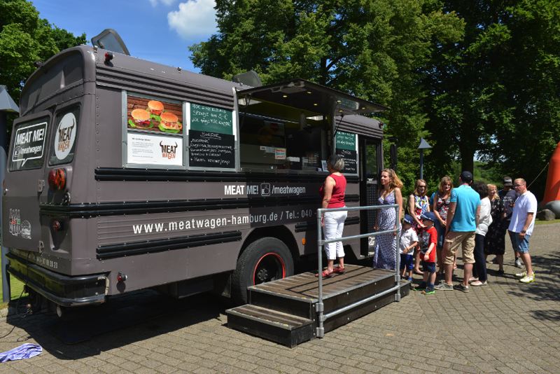 Ein Food Truck mit dem Namen 'Meat Me' und einer Warteschlange von Menschen, die auf Essen warten.