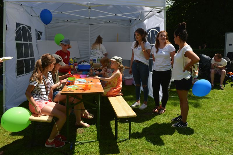 Kinder und Betreuer:innen basteln an einem Tisch unter einem Pavillon im Freien.