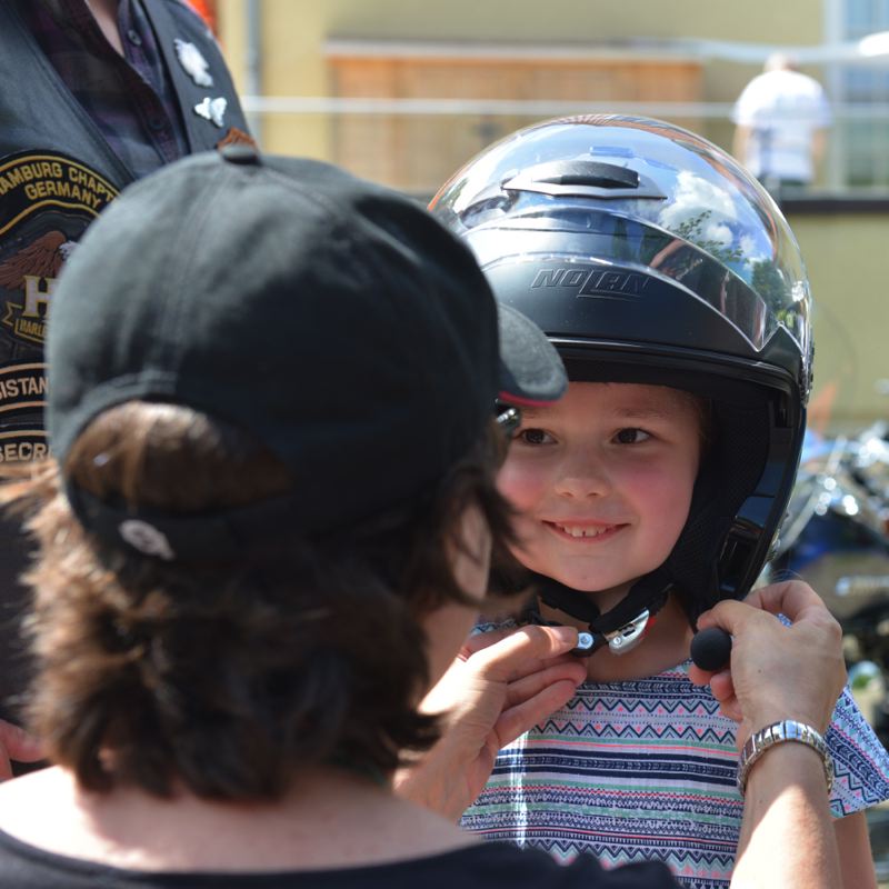 Ein Kind trägt einen Motorradhelm und wird von einer Person dabei unterstützt, ihn zu zumachen.