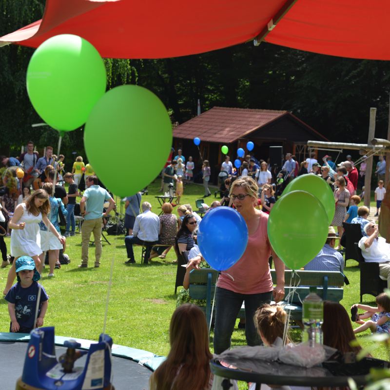 Menschen auf einem Sommerfest mit grünen und blauen Luftballons in einem Garten.