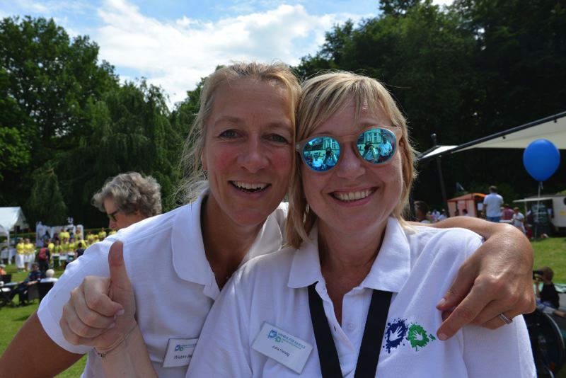 Zwei Frauen lächeln in die Kamera, eine zeigt den Daumen nach oben, beide tragen weiße T-Shirts.