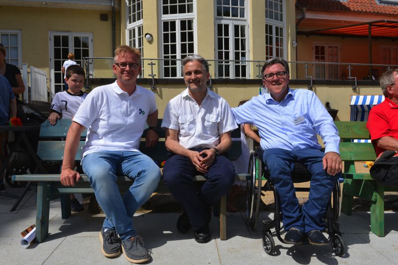 Drei Männer sitzen nebeneinander im Freien.