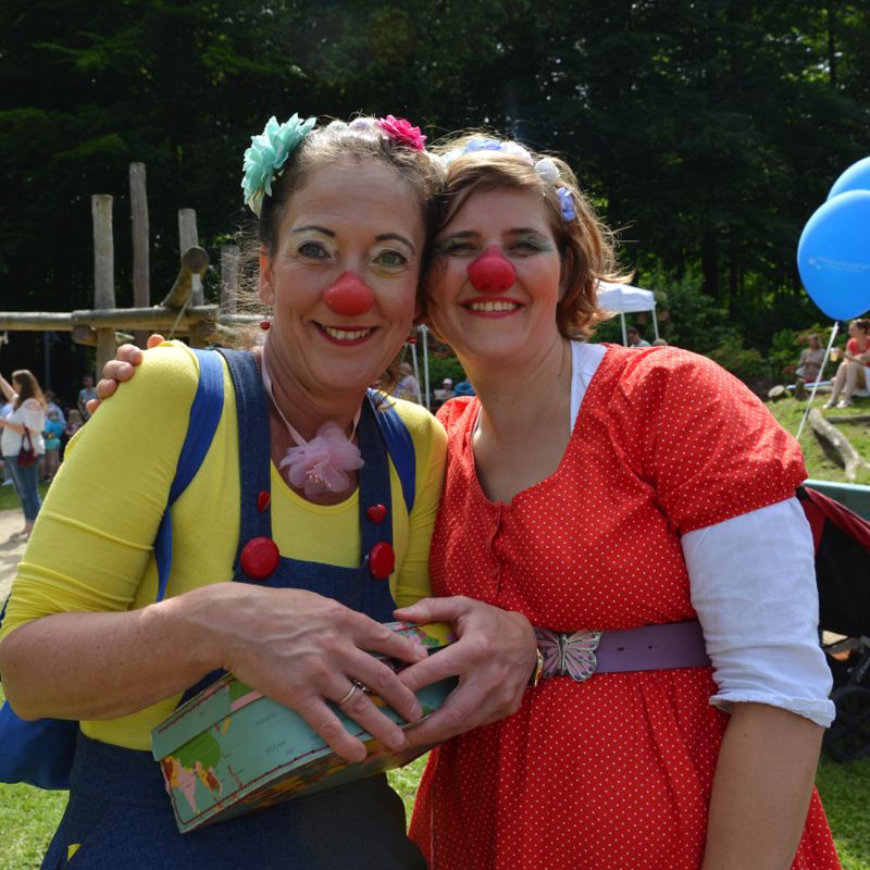 Zwei Clowns mit roten Nasen und bunten Kostümen posieren für ein Foto bei einem Fest.