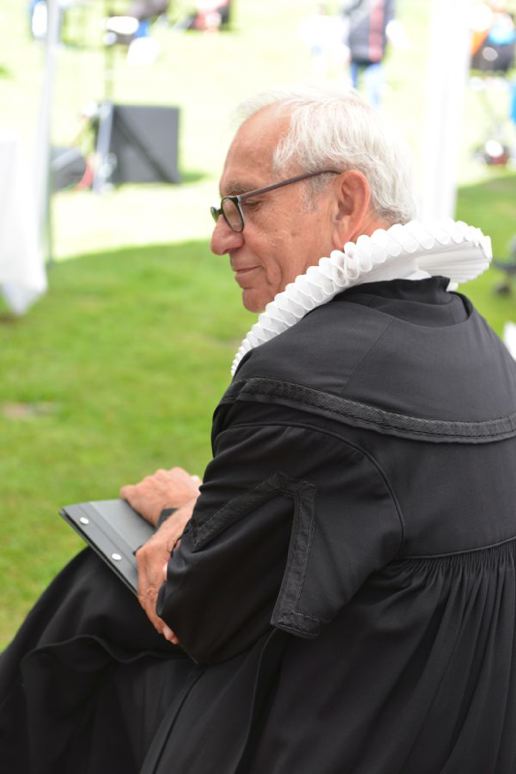Ein Pastor in einer schwarzen Robe mit einem weißen Kragen sitzt mit einem Notizblock in der Hand.