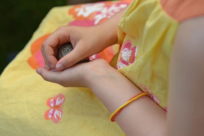 Ein Kind hält einen Stein in den Händen, während es ein gelbes Kleid mit Blumenmuster trägt.