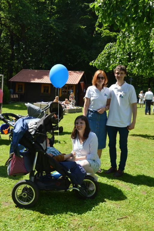 Eine Gruppe von Menschen, darunter ein Kind im Kinderwagen mit einem blauen Ballon, auf einer Wiese.