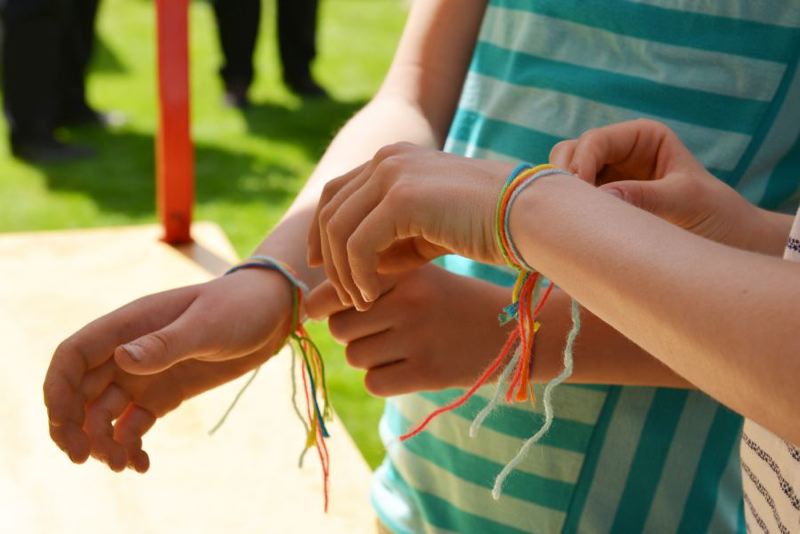 Zwei Kinderhände mit bunten, geflochtenen Armbändern in verschiedenen Farben.