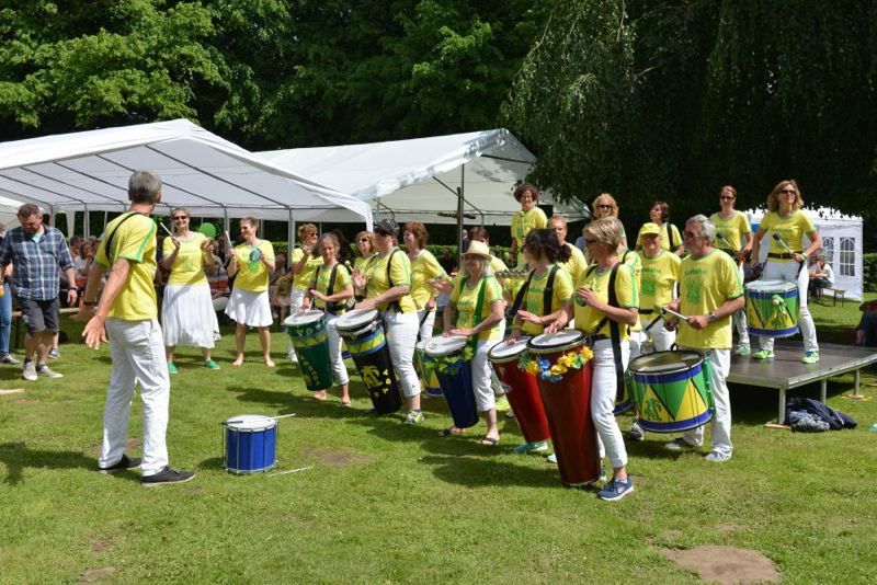 Eine Trommelgruppe in bunten Outfits spielt auf einem Sommerfest im Freien.