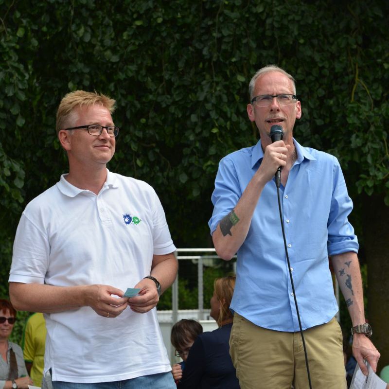 Zwei Männer stehen nebeneinander, einer spricht ins Mikrofon, während der andere zuhört.