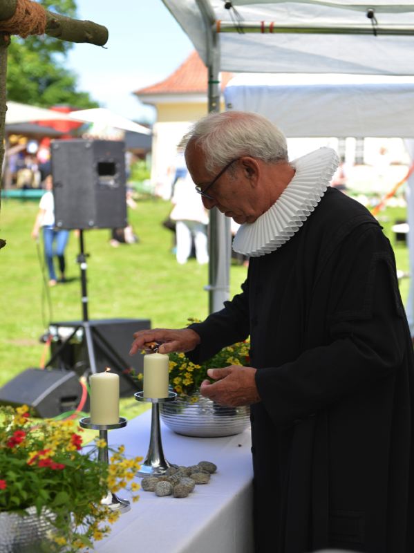 Ein Pastor in schwarzem Gewand zündet Kerzen an einem Tisch mit Blumen an.