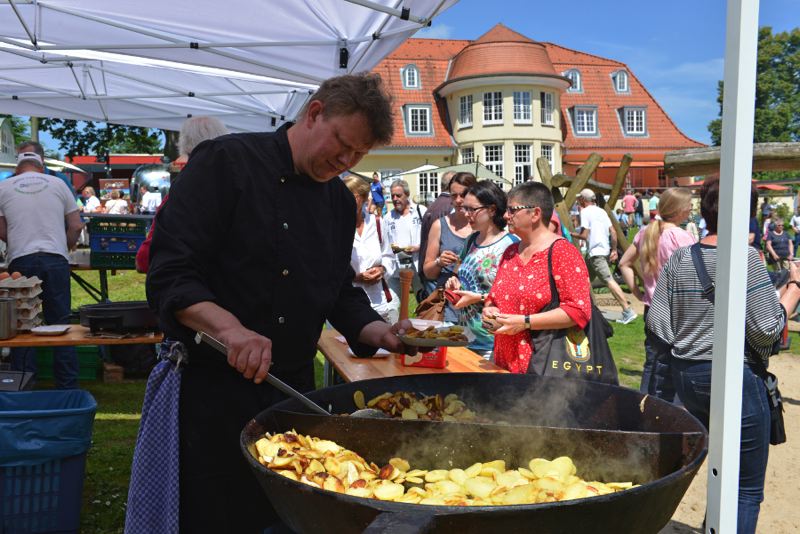 Ein Koch bereitet gebratene Kartoffeln in einer großen Pfanne während eines Sommerfestes vor.