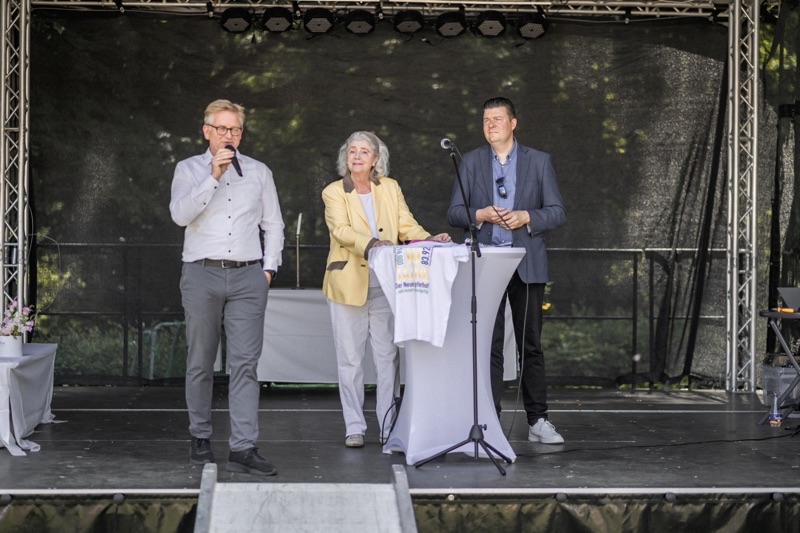 Zwei Männer und eine Frau stehen auf einer Bühne während einer Veranstaltung.